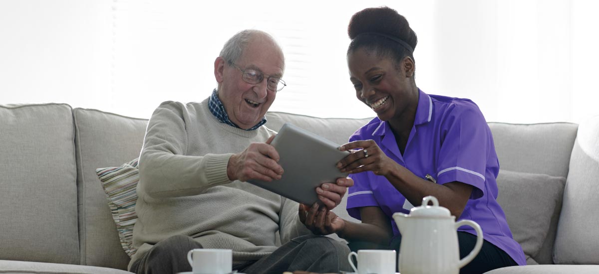 Carer and service user sitting on a sofa laughing together