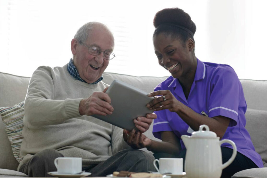 Carer sitting on a sofa with a resident looking at a tablet