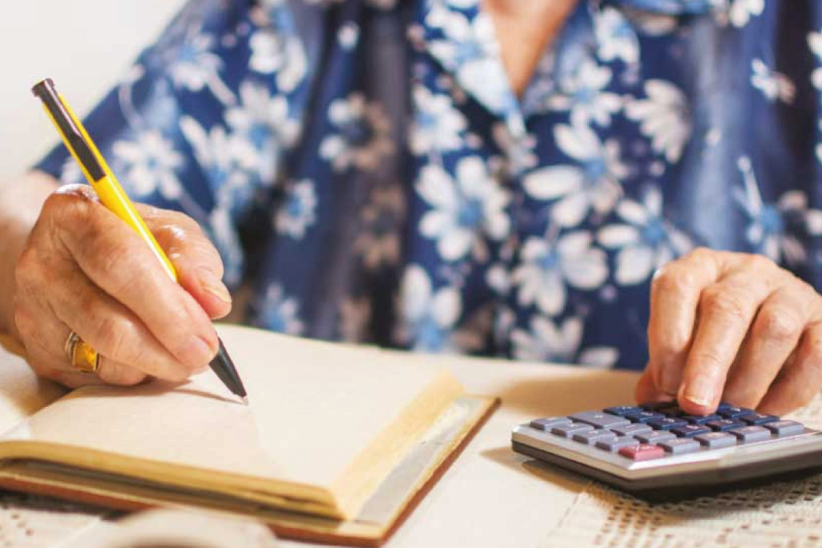 Elderly person writing on a notepad and using a calculator