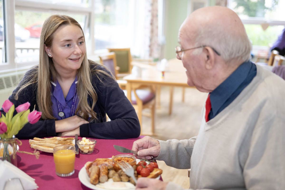 Care home Resident sitting at a table with a Care Worker eating a freshly prepared meal