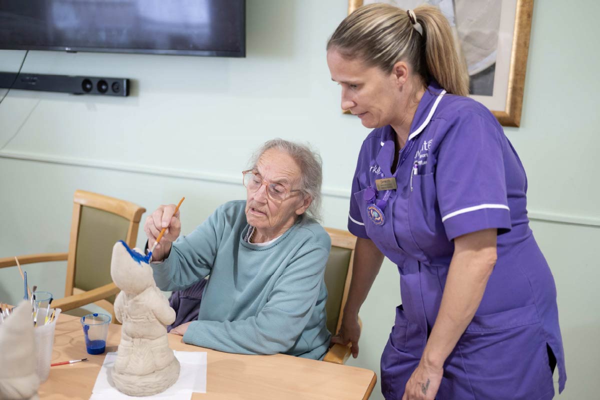 Resident enjoying an activity of painting a garden gnome with the help of an Avante Care Worker