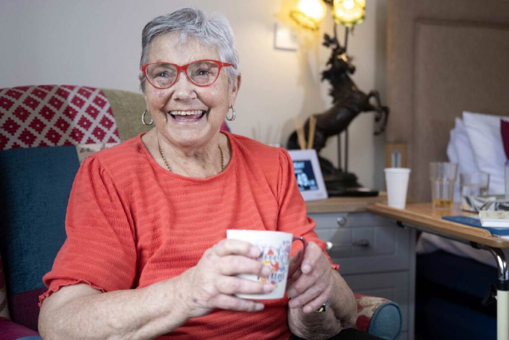 A resident smiling and holding a cup of tea