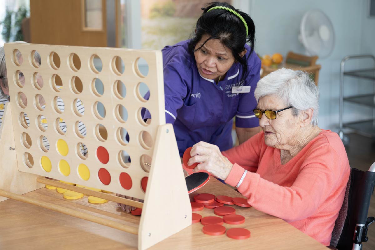 An Avante staff member helping a resident play Connect Four